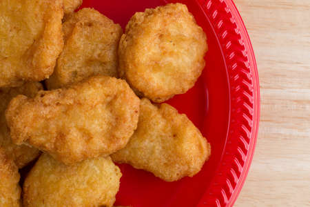Top close view of a serving of chicken nuggets on a red plate on a wood table top illuminated with window light.の写真素材