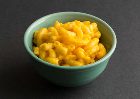 A small bowl of macaroni and cheese on a dark background illuminated by window light.の写真素材