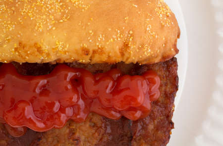 A very close view of a pork rib sandwich with ketchup added on a white paper plate.の写真素材