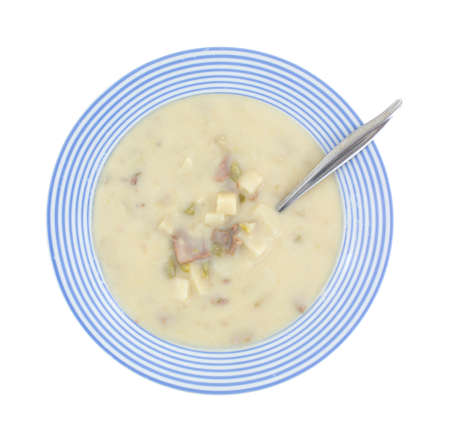 Top view of a bowl of creamy cheesesteak soup in a blue striped bowl with a spoon on a white background.の写真素材