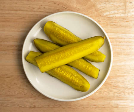 Top view of several bread and butter pickle spears on a small plate atop a wood table top illuminated by window light.の写真素材