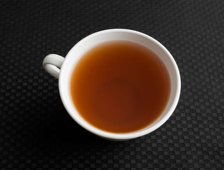 A cup of passion fruit green tea atop a black tablecloth.の写真素材