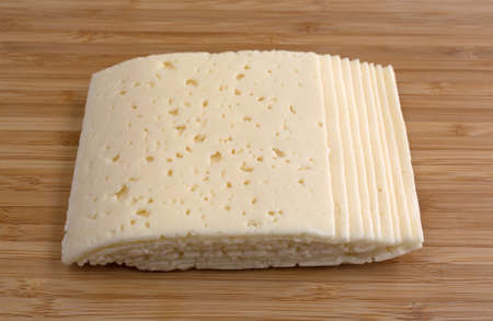 Several slices of Havarti cheese on a wood cutting board illuminated with natural light.の写真素材