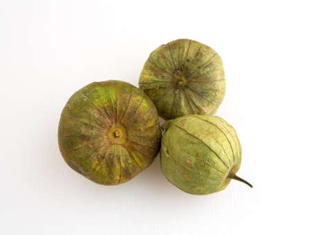 Three ripe tomatillos on a white cutting board illuminated with natural light.の写真素材