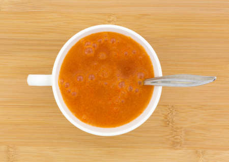 A white cup filled with water and orange fiber laxative on a wood table top.
