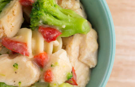Top close view of a serving of grilled chicken with assorted vegetables in a garlic sauce in a bowl atop a wood table top.の写真素材