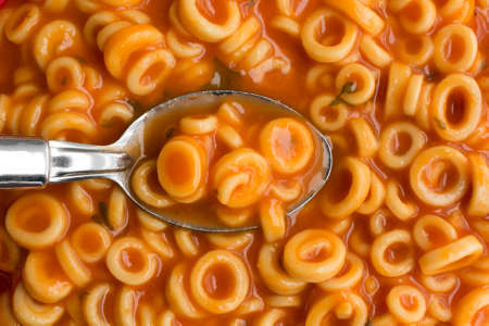 A very close view of canned round spaghetti pasta with tomato sauce in a spoon illuminated by natural light.の写真素材