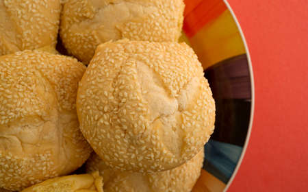 Top close view of sesame seed bulky rolls on a colorful plate atop an orange table top.