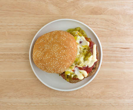 Top view of a cheeseburger with sesame seed bun plus mayonnaise, ketchup and relish on a small plate atop wood table.の写真素材