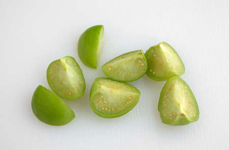 Top view of several sections of cut tomatillos on a white cutting board.の写真素材