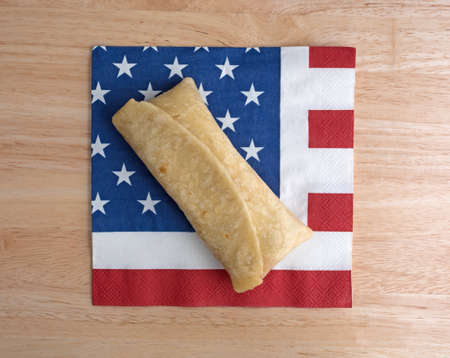 Top view of a microwaved chimichanga on an American flag motif napkin atop a wood table top.