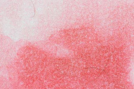 A very close view of red watercolor paint on textured paper with several bristles from an...