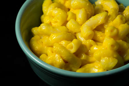 A close view of a small bowl filled with macaroni and cheese atop a black velvet tablecloth.