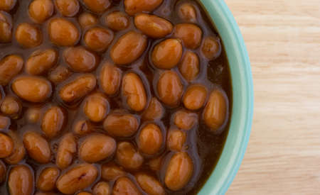 Close view of a bowl of country style baked beans in a small bowl atop a wood table top.