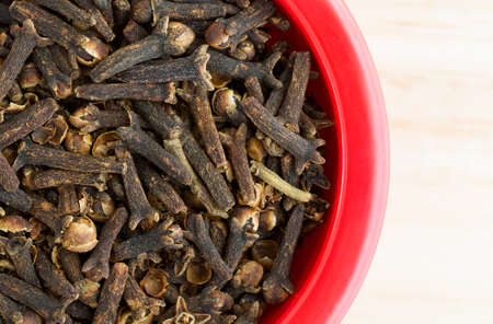 Top close view of a red dish filled with whole cloves on a wood counter top.の写真素材