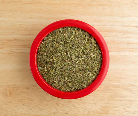 Top view of a red dish filled with Italian seasoning on a wood counter top illuminated with natural light.の写真素材