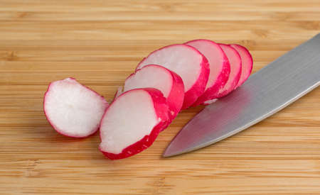 A sliced radish on a wood cutting board with a knife illuminated with natural light.の写真素材