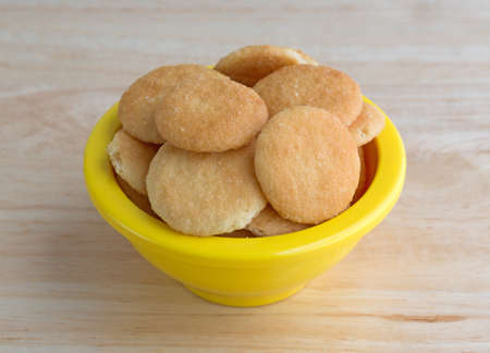 A small yellow bowl filled with vanilla flavored wafer cookies on a wood table top illuminated with natural light.の写真素材