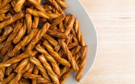 Top close view of a plate filled with braided pretzels atop a wood table top illuminated with...