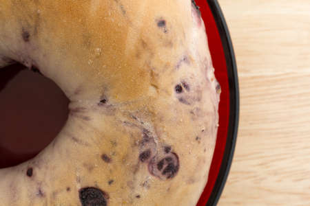 Top close view of a freshly baked blueberry bagel on a small red dish atop a wood table top.の写真素材