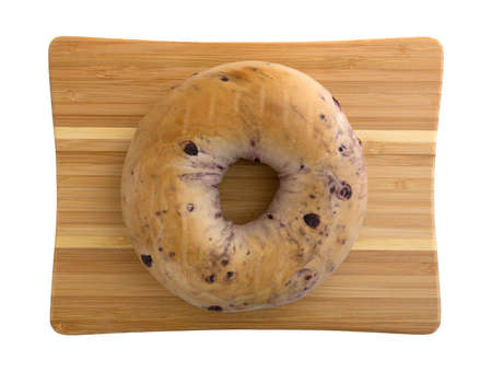 Top view of a freshly baked blueberry bagel on a small wood cutting board isolated on a white background.の写真素材