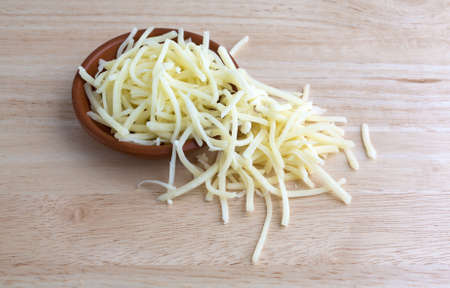 A portion of natural mild cheddar cheese spilling from a small bowl atop a wood table top illuminated with natural light.の写真素材