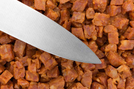 A knife atop pepperoni pizza topping that has been chopped into small cubes.