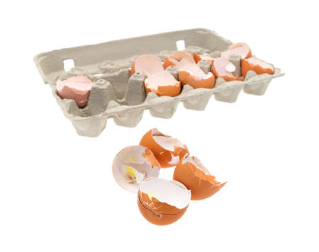 A group of broken and used eggs in the foreground with the remainder in a cardboard carton in the...