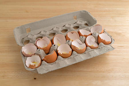 A dozen broken eggshells in an opened cardboard container on a wood counter top illuminated with...