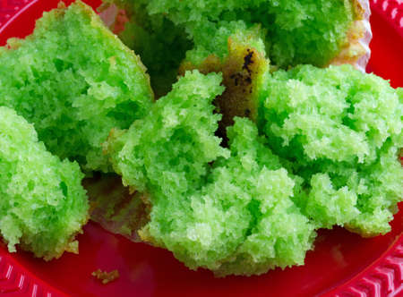 Close view of a freshly baked pistachio breakfast muffin that has been broken into several pieces on a red plastic plate.の写真素材