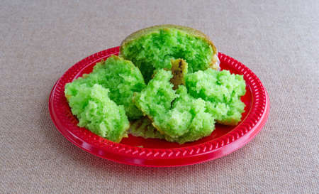 A freshly baked pistachio breakfast muffin that has been broken into several pieces on a red plastic plate atop a burlap tablecloth.の写真素材