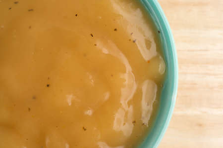 Top close view of a green bowl with chicken flavored gravy on a wood table illuminated with natural light.の写真素材