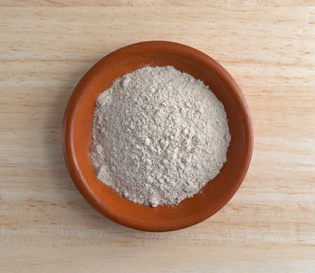 Top view of a small bowl with a portion of dry brown gravy mix on a wood counter top illuminated...