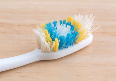 An old worn toothbrush with bent bristles on a wood counter top illuminated with natural light.