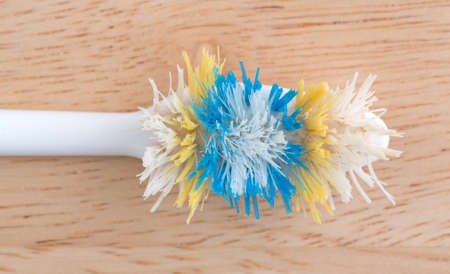 Top view of an old worn toothbrush with bent bristles on a wood counter top illuminated with natural...