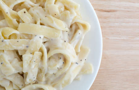 Top close view of a fettuccine alfredo TV dinner on a plate on a wood table top illuminated with natural light.の写真素材
