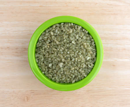 Top view of a small bowl filled with green gluten free bamboo rice on a wood table top illuminated with natural light.の写真素材