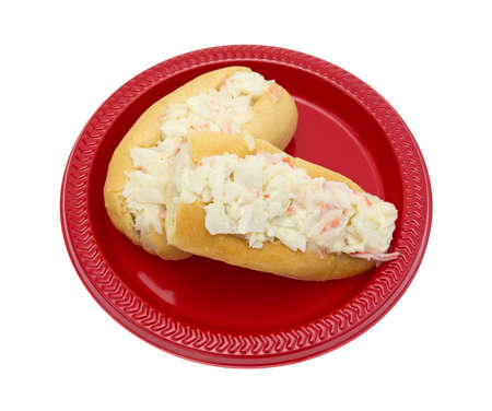 Two small surimi crab meat made into a salad with mayonnaise on small sub rolls atop a red plastic plate isolated on a white background.の写真素材