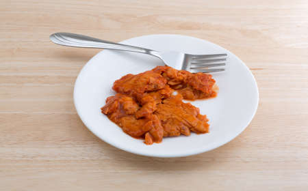 Side view of a small portion of spicy flavored pink salmon on a plate with fork atop a wood table...