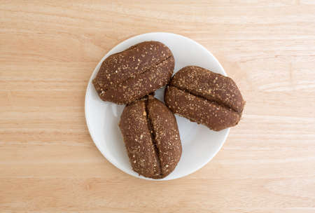 Top view of three freshly baked multi-grain rolls on a white plate atop a wood table top illuminated with natural light.の写真素材