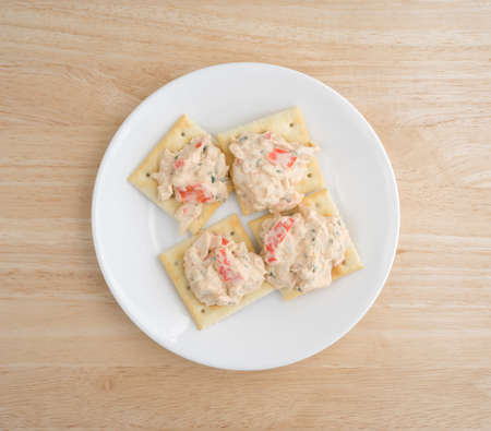 Top view of a plate of saltine crackers with lobster snack dip atop a wood table top.