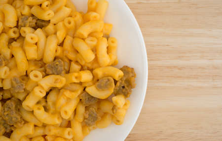 Top close view of macaroni and cheese with hamburger chunks on a white plate atop a wood table top.の写真素材