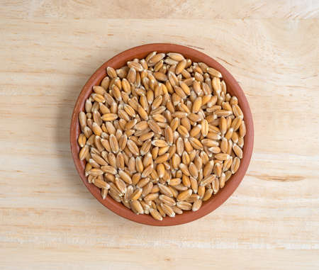 Top view of a small bowl filled with organic whole grain spelt on a wood table top illuminated with natural light.の写真素材