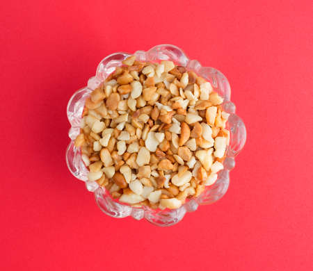 Top view of roasted and salted macadamia nut pieces in a glass bowl atop a bright red background.