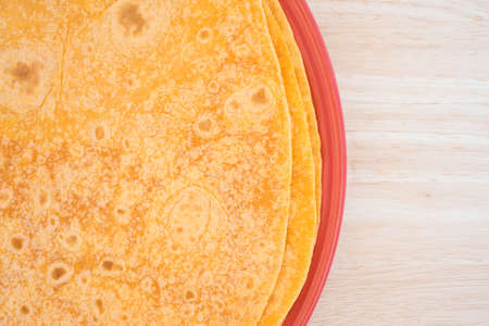 Top close view of several tomato tortilla wraps on a plate atop a wood table top.の写真素材