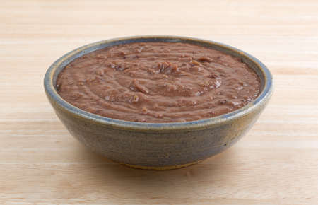 Side view of a bowl filled with black bean dip atop a wood table top.