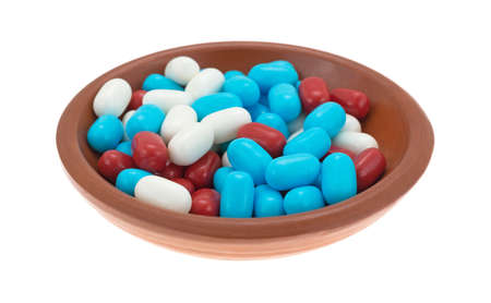 Side view of an assortment of red white and blue breath mints in a small bowl isolated on a white...