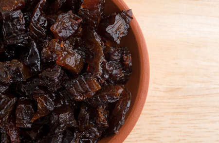 Top close view of a portion of diced prunes in a small bowl atop a wood table top.の写真素材