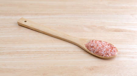 A portion of Himalayan pink salt on a large kitchen spoon on a wood counter top.の写真素材