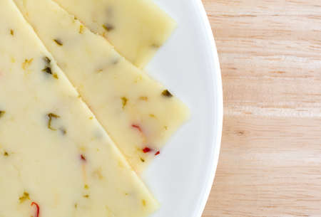 Top close view of pepper jack cheese slices on a white plate atop a wood table top.の写真素材